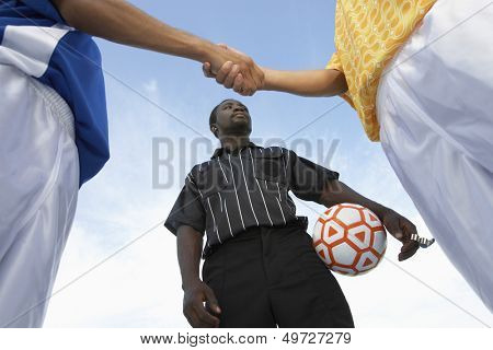 Low angle view of referee with opponent team players shaking hand against sky
