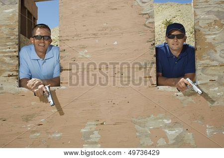 Two men holding hand guns at firing range, portrait