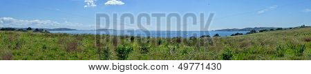 Panoramic View Over Meadows With Bushes In Front Of The Sea Behind