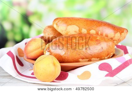 Fresh baked pasties with fruit jam, on wooden table, on bright background