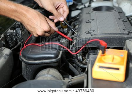 Auto mechanic uses multimeter voltmeter to check voltage level in car battery