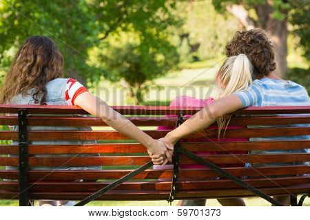 Rear view of a man with girlfriend while holding hands with another woman in the park