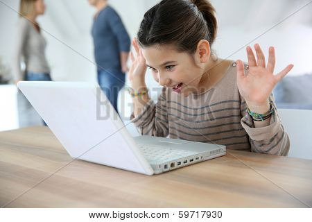 Young girl at home cwaving at laptop webcamera