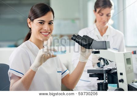 Portrait of young female researcher holding slide while using microscope in laboratory
