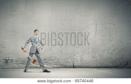 Young determined businessman in suit holding big axe