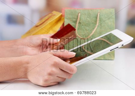 Female hands holding credit card with computer tablet and paper bags on table on bright background