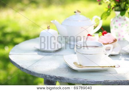 Coffee table with teacups and tasty cakes in garden