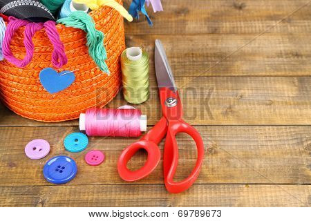 Round orange box full of multicoloured thread and everything necessary for sewing on wooden background