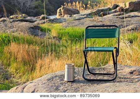 Camp chair and thermos cup on nature background