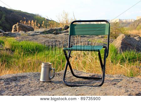 Camp chair and thermos cup on nature background
