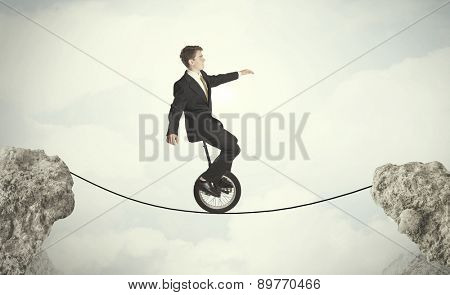 Brave business man riding an mono cycle between cliffs concept