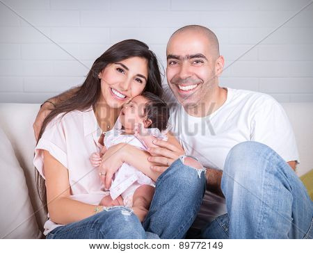 Portrait of happy cheerful family sitting on the couch at home, young parents enjoying time spent with their adorable newborn daughter