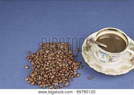 coffee mug on the table with a blue tablecloth, poured out coffee beans
