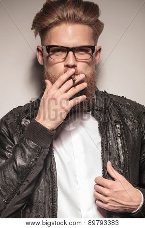 Close up portrait of a blond hipster business man smoking a cigarette while fixing his jacket.