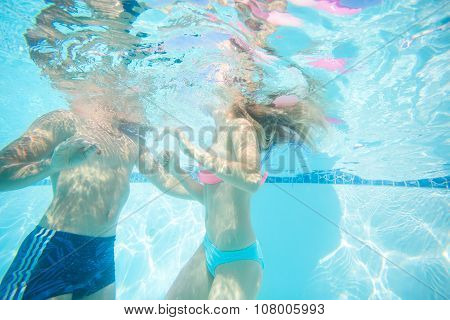 Young couple swimming underwater in pool.
