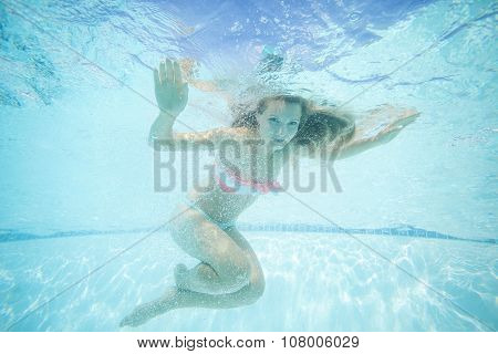 Beautiful young woman swimming underwater in pool.
