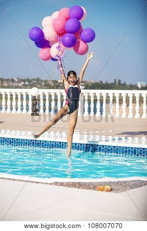 Joyful girl jumping into the pool while holding a bunch of balloons