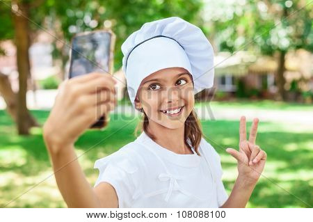 Happy girl in chef's hat making selfie.