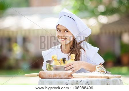 Smiling little chef showing ducklings in a bowl while cooking.