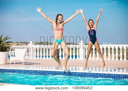 Young mother and daughter jumping into the swimming pool and screaming of joy.