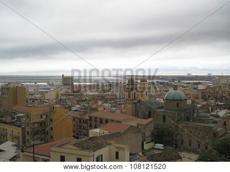 Cagliari's Skyline With Buildings, Port, Sea And Gloomy Grey Cloudy Sky