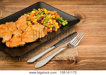 Pork tenderloin slices stewed in  tomato sauce with vegetables on the black plate  on the rustic bac