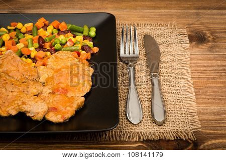 Pork tenderloin slices stewed in  tomato sauce with vegetables on the black plate  on the rustic bac