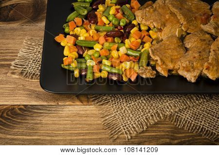 Pork tenderloin slices stewed in  tomate sauce with vegetables on the black plate  on the rustic bac