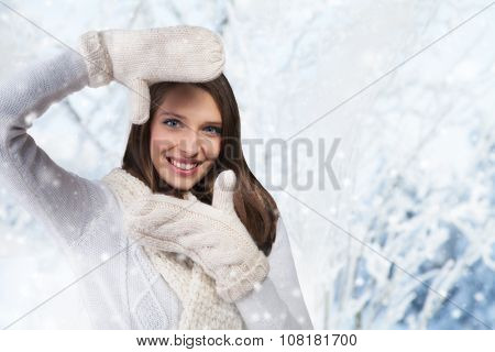 Beautiful winter portrait of young brunette woman showing photo frame guesture in the winter snowy scenery