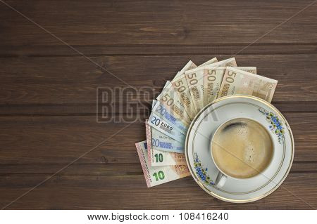 Cup of coffee and money. Valid banknotes on a wooden table.