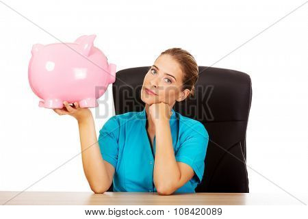 Young female doctor or nurse holding piggybank.