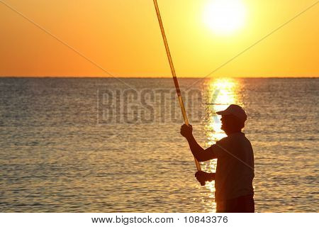 Man steht am Ufer mit Angelrute und Fische auf Sonnenuntergang