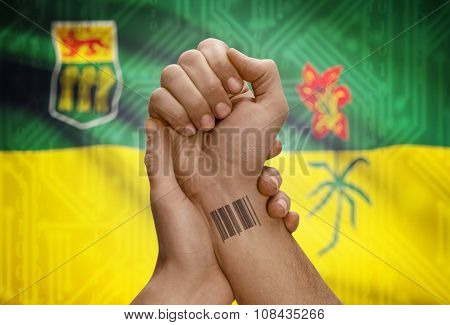Barcode Id Number On Wrist Of Dark Skin Person And Canadian Province Flag On Background - Saskatchew