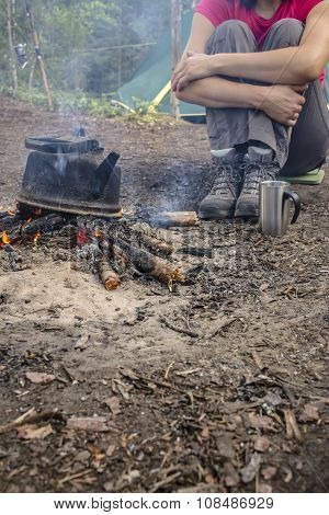 Girl Sitting While Camping Near The Fire Heated And Drink Hot Tea