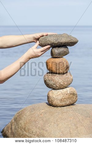 Human Hand Making Stack Of Large Round Stones Near The Water