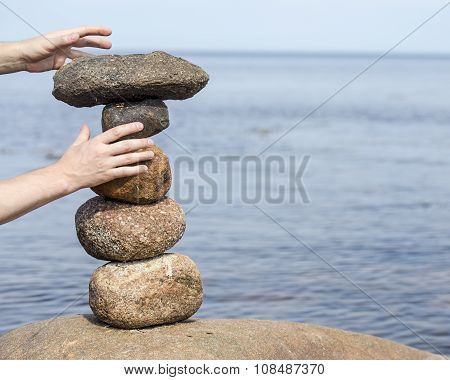 Human Hand Making Stack Of Large Round Stones Near The Water