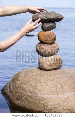 Human Hand Making Stack Of Large Round Stones Near The Water