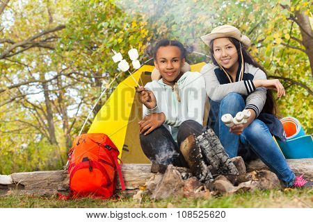 Girls hold marshmallow sticks near fireplace