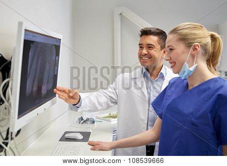 people, medicine, stomatology, technology and health care concept - happy dentists looking to x-ray scan on monitor at dental clinic