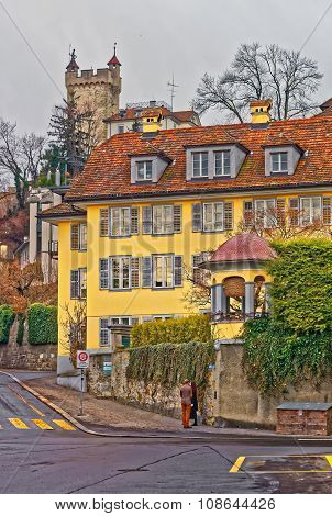 Unidentified young couple at the corner of a beautiful bright yellow house in the swiss city of Lucerne. A tower of the Musegg Wall (800 meter long city fortification) seen in the background.