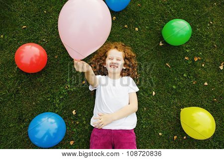Happy Little Girl Holding Colored Balloon, Lies On Green Grass At Summer Park.