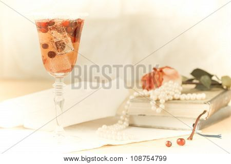 Glass Of Champagne And Cranberry Cocktail With Vintage Books And Pearls