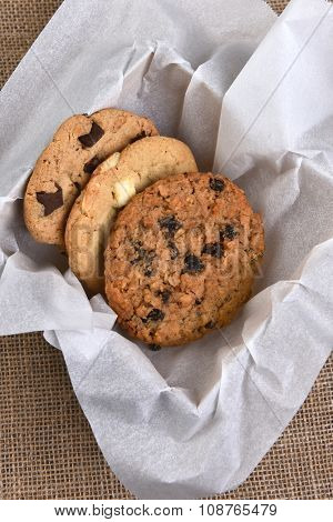 High angle view of a box of assorted gourmet cookies. Chocolate, oatmeal raisin and white chocolate chip cookies closeup in a box stuffed with paper on a burlap surface.