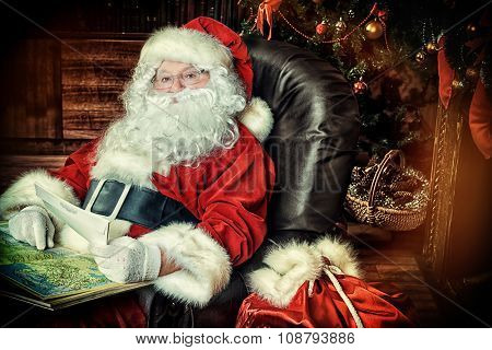 Santa Claus reading letters from children and looking at the world map. He is at home, decorated for Christmas. Santa's mail.