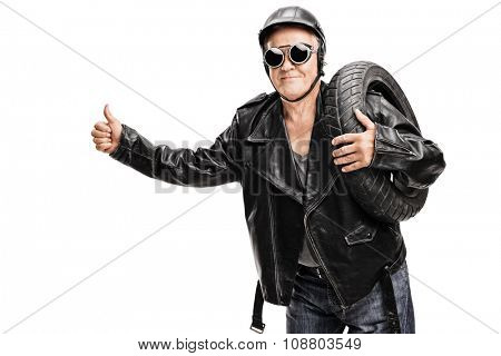 Senior biker in a black leather jacket carrying a tire and hitchhiking with his thumb isolated on white background