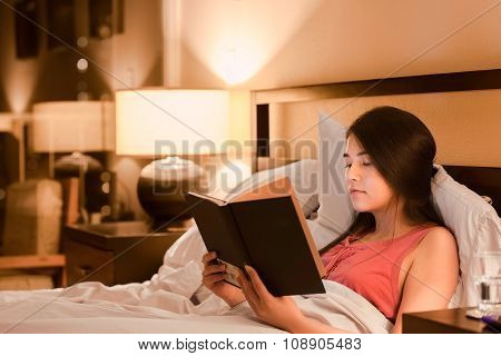Biracial Teen Girl Reading Book  In Bed At Night