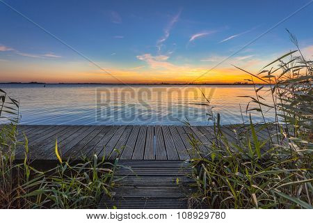 Blue And Orange Sunset Over Boardwalk On The Shore Of A Lake