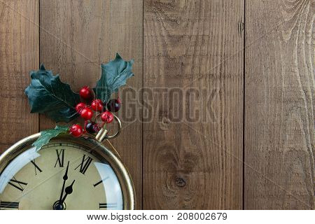 Christmas vintage clock with Holly berries on a wood background. Part of clock showing. Time almost 12 o'clock almost Christmas! Vintage traditional warm brown colors with bright red berries. Lots of copy space.