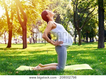 Side view of relaxed pregnant woman doing yoga on mat in park. Health care 