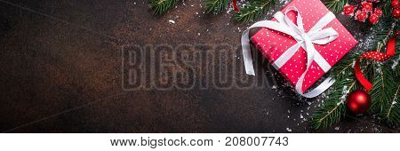 Christmas background or greeting card. Christmas red present box fir tree and decorations on dark stone table. Top view. Long banner format.